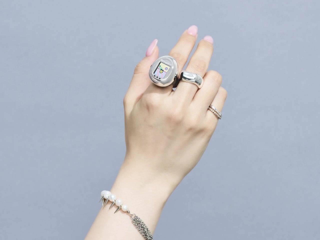 Tamagotchi Ring 메인 이미지, 손가락에 착용한 실버 컬러 반지형 다마고치
