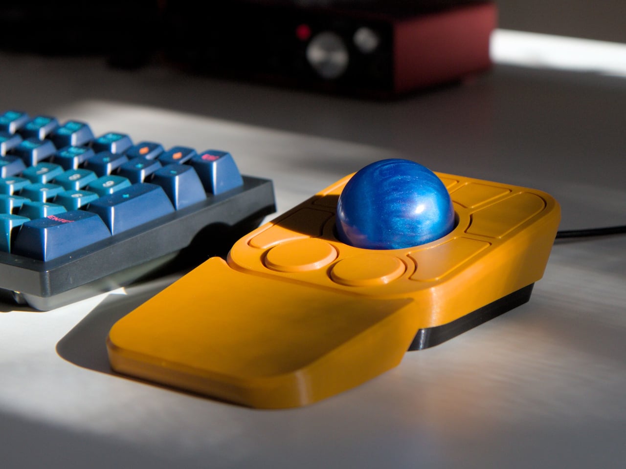 Ploopy Adept+ main image, an orange trackball sitting next to a mechanical keyboard